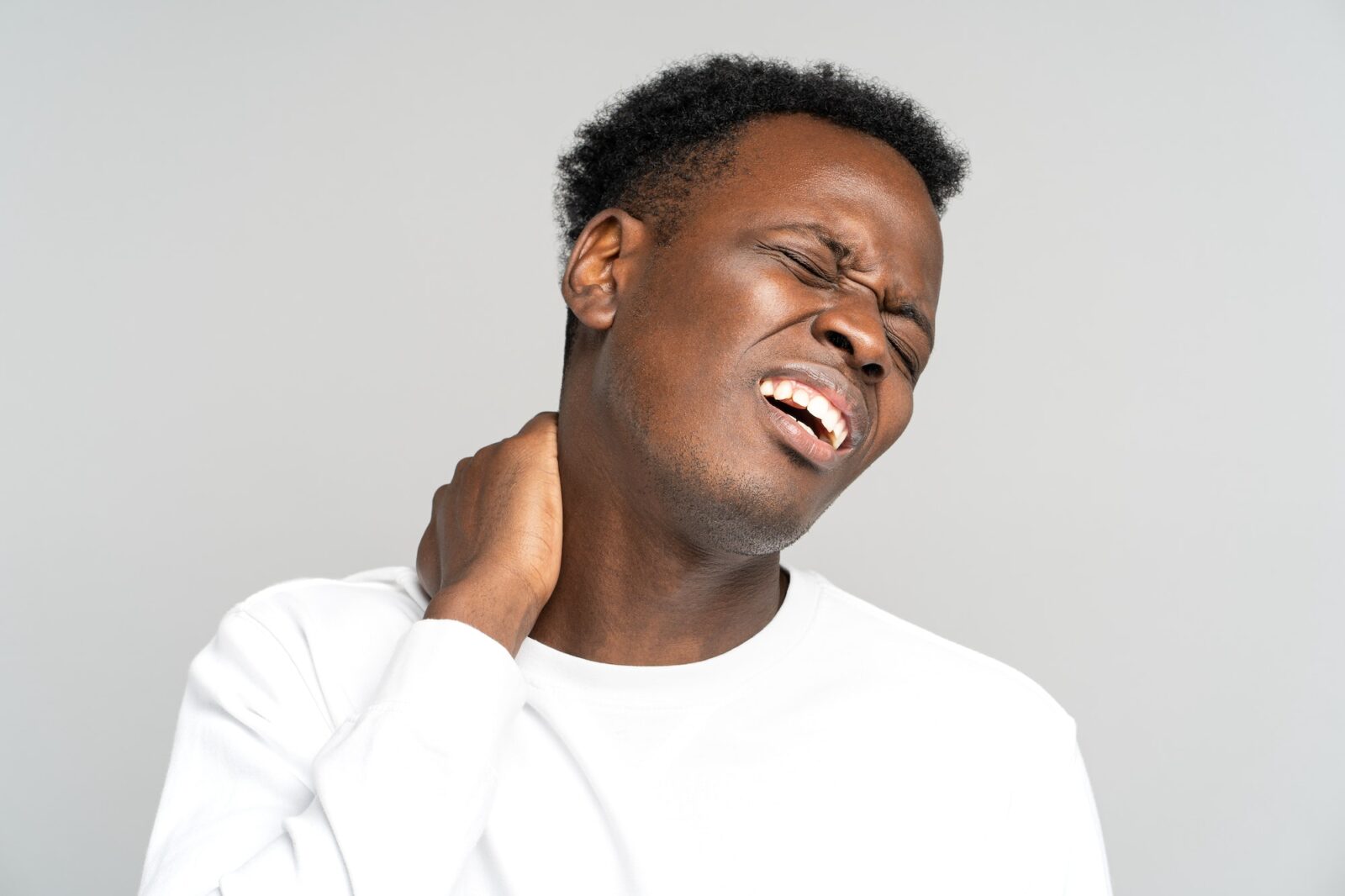 Unhappy Black man suffering from neck pain, pinched nerve in her back, has spinal problem. Studio.
