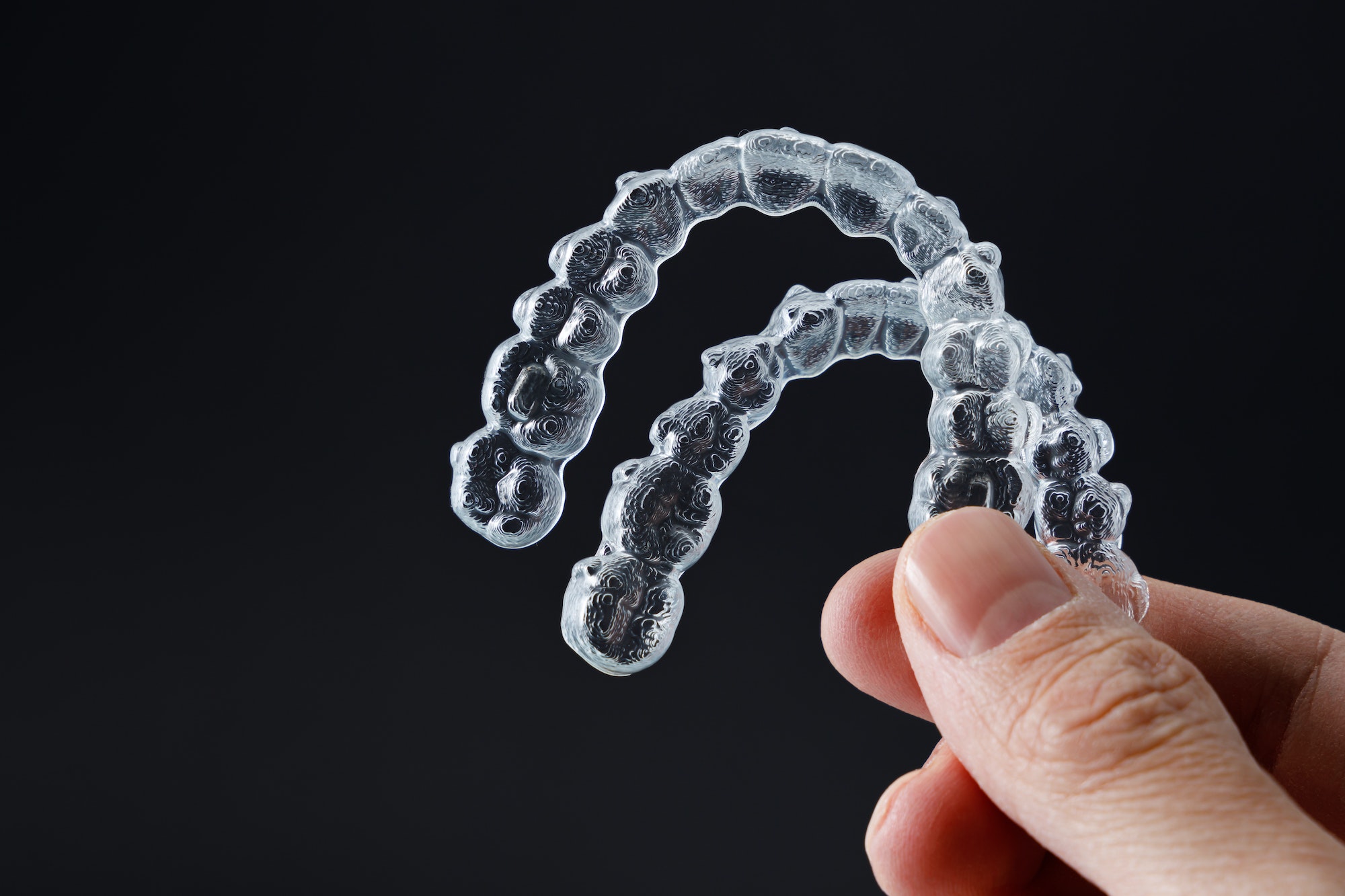 Clear aligner trays held between fingers, representing Invisalign and ClearCorrect orthodontic treatment options